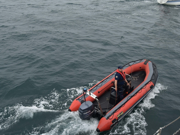 Pendant le contrôle, un douanier reste à bord du pneumatique à proximité du bateau. Nautisme Article