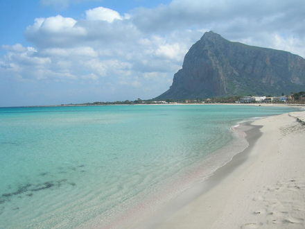 La couleur de l'eau varie du bleu clair au bleu foncé et le contraste avec les montagnes et les falaises gris brun qui se dressent derrière le sable crée un spectacle magnifique.